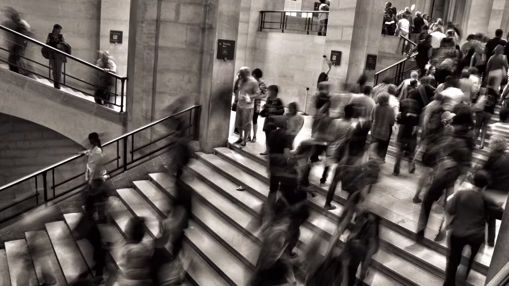 Black and white photo of a busy staircase at a train station with people rushing by.